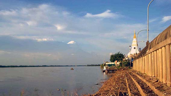 Au loin sur le Mékong, la pointe de l'ancien stupa immergé fait face à sa réplique moderne érigée sur la rive.
